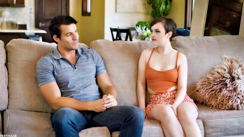 Jade Valentine in orange top and skirt sitting with muscular tutor on couch