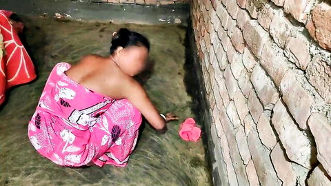 South Asian woman in pink saree bends over exposing bare back and ass cheeks on dirty floor