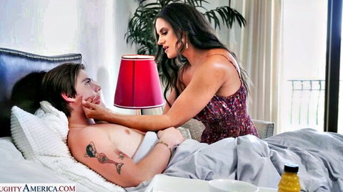 Brunette MILF in dress caresses shirtless young guy's chest and face in bed