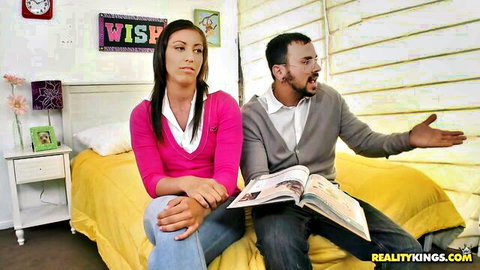 Sexy long-haired brunette in pink sweater sits on bed with bearded guy gesturing over open book