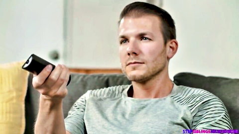 Handsome stepbrother in striped shirt holds remote, pranking stuck stepsis