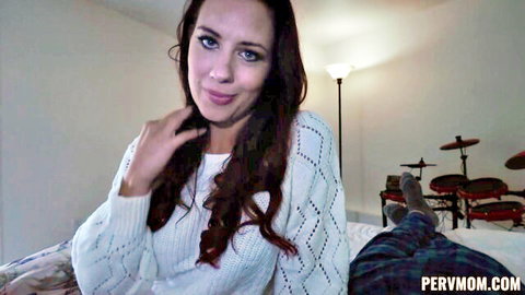 Seductive redhead MILF in white knit sweater smiles teasingly on bed with stepson