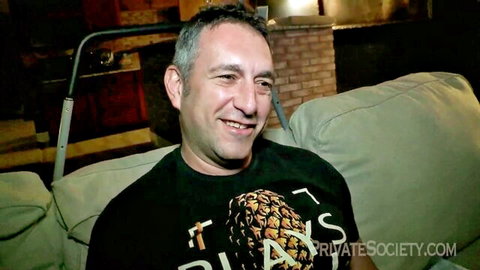 Smiling middle-aged man in black pineapple Private Society t-shirt lounging on couch