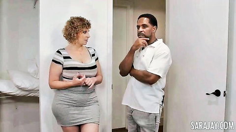 Busty curly blonde MILF in low-cut striped top and tight skirt chats with muscular black stud in bedroom