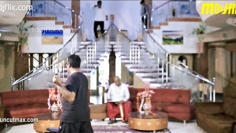 South Asian men in casual clothes gather in luxurious Indian home with grand glass stairs and red sofas