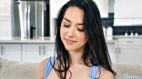 Brunette beauty in tight blue tank top smiling seductively on kitchen couch