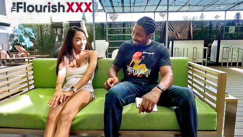 Sexy Asian babe in skimpy white top and shorts flirting with dreadlocked black stud on green patio couch