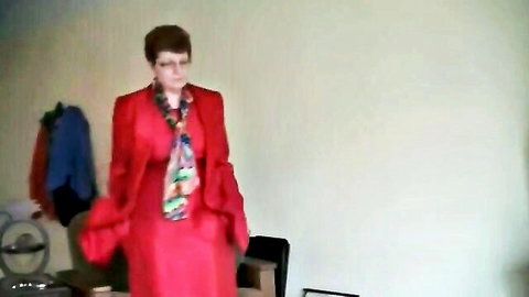 Mature short-haired redhead granny in red suit and colorful scarf posing clothed in office