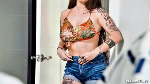 Tattooed babe teasing in sheer floral halter top and tiny denim shorts showing cleavage