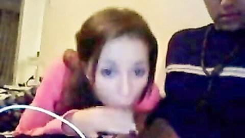 Brunette girlfriend in pink top puckers lips toward boyfriend's crotch on webcam