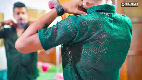 Shirtless Indian man adjusting green embroidered shirt in mirror