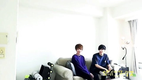 Two cute Asian twinks sitting on couch in bedroom smiling for gay couple foreplay
