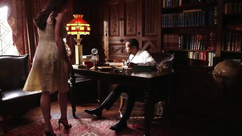 Alyx Star in short dress bending over desk with man in library scene