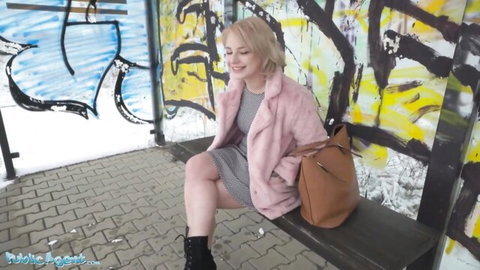 Smiling blonde in pink fur coat and short dress at snowy bus stop
