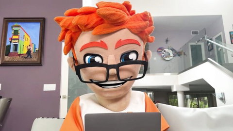 Savvy Suxx in casual orange top with red hair and glasses at home