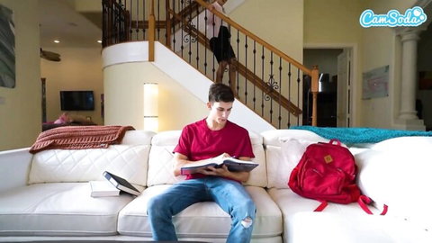 Young stepson reads book on couch while stepmom teases up stairs in skirt