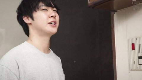 Handsome smiling Japanese guy in gray t-shirt standing in kitchen near intercom
