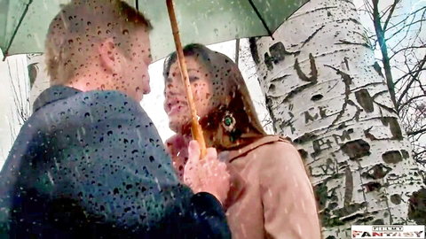 White man passionately kissing sexy Asian woman under green umbrella in rainy birch forest