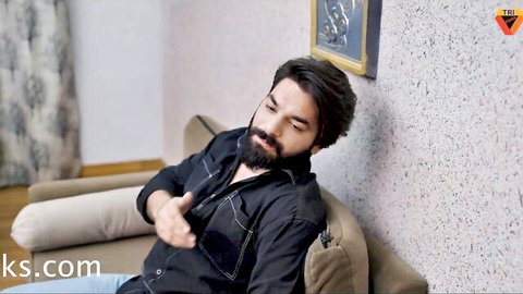 Bearded Indian man in black shirt lounging on couch, teasing gesture for hardcore session