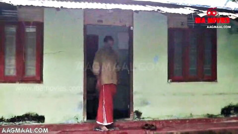 Desi man in beige shirt and red lungi stands at rural green house door