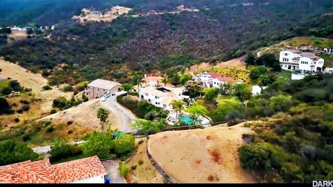 Aerial drone view of luxury white villas with red tile roofs on dry sunny hillside and pool