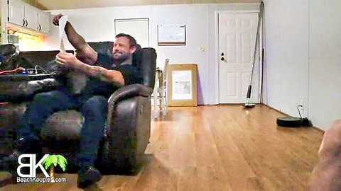 Shirtless tattooed man with sweaty face holds white towel stretched in black recliner living room