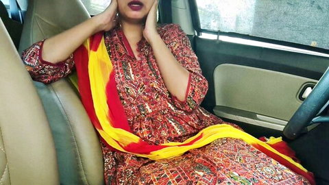 Indian wife in red dress and yellow dupatta sits in car, teasing expression