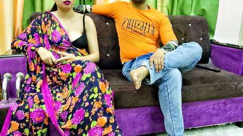 Sexy Indian woman in revealing floral saree showing black bra cleavage sits with arm-around boyfriend on couch