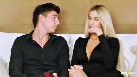Skinny blonde with small tits in deep cleavage black dress flirts with young guy on bed