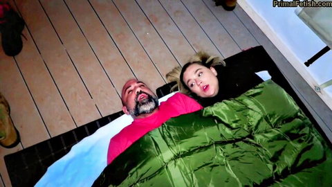 Young blonde teen surprised face as DILF daddy smiles intimately under green sleeping bag on floor