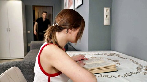 Bella Gray in tank top reading, step-dad lurking behind in homemade domination setup