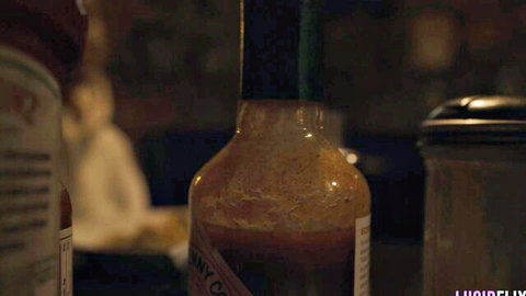 Ryan Reid in dimly lit diner with hot sauce bottles, teasing vibe
