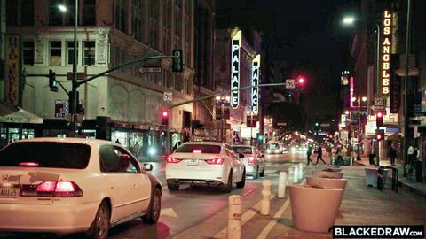 Nighttime Los Angeles street scene with Palace neon signs, traffic lights, cars stopped at intersection and pedestrians