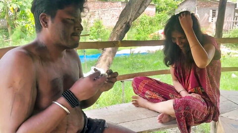 Shirtless Indian man and woman in colorful dress sit outdoors, naughty vibe