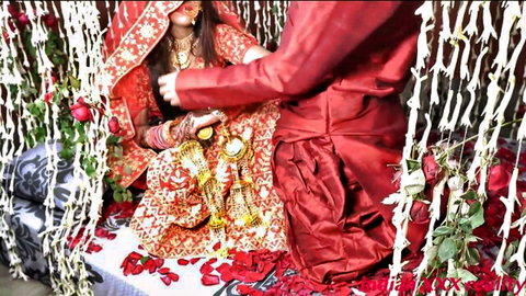 Shy Indian bride in red lehenga sits as groom caresses her thigh in romantic wedding night tease