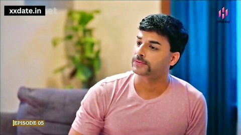 Handsome mustached Indian man in pink t-shirt sitting on couch looking aside in homemade video