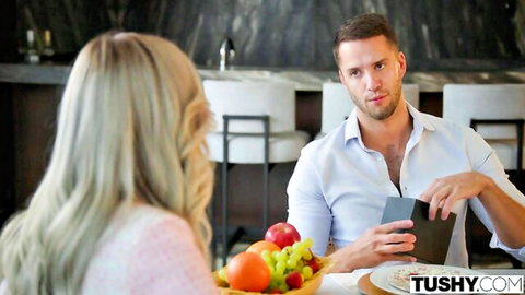Blonde woman with long hair in pink top facing handsome man holding phone at kitchen fruit table