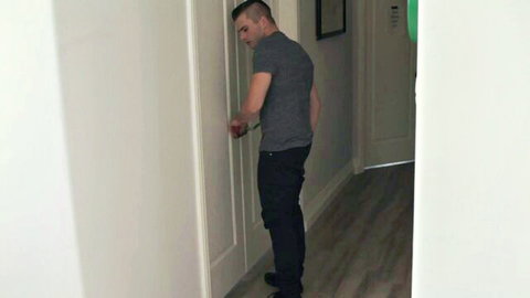 Muscular man in gray t-shirt and jeans opening bedroom door in hallway