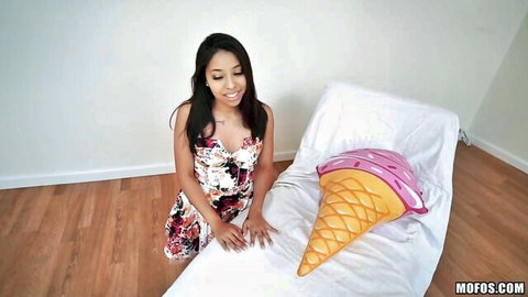 Brunette in short floral dress bends over bed teasing giant pink ice cream pillow