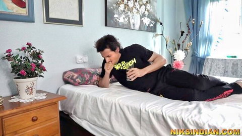 Young Indian guy in black Raksh t-shirt lying on bed in amateur bedroom