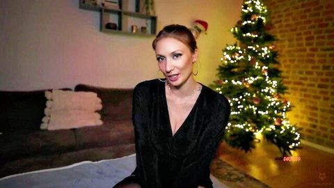 Sexy blonde in Santa hat teases with tongue out showing deep cleavage by Christmas tree