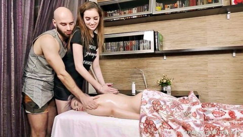 Bald man and brunette masseuse oil shiny naked ass of woman on massage table in threesome
