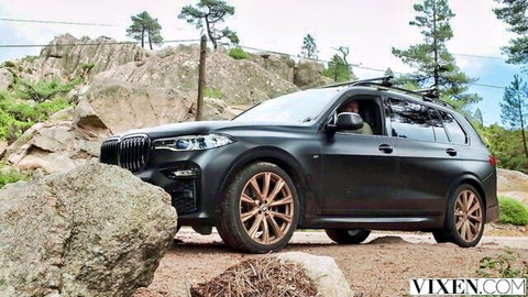 Black BMW X7 SUV off-roading on rocky forest path with pine trees