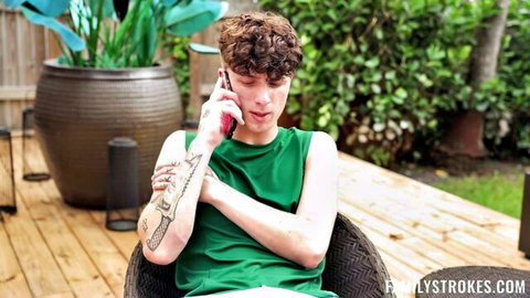 Tattooed curly-haired guy in green tank top talking on phone outdoors on patio
