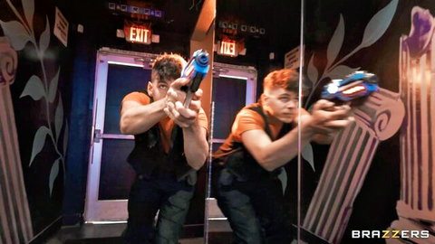 Two muscular men in laser tag vests aim neon guns in mirrored arena with exit doors