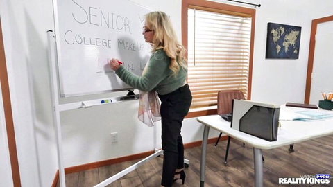 Blonde Maisey Monroe in green top and pants writing on board in college scene