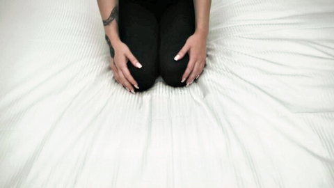Petite brunette kneeling in black leggings on bed, tattooed arms, POV tease