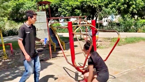 Busty Indian woman in black dress squats outdoors with man watching in park