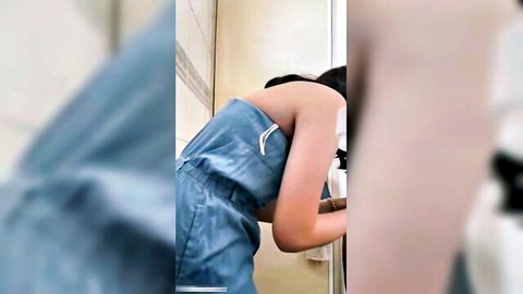 Young Asian woman in blue strapless dress bending over in bathroom mirror