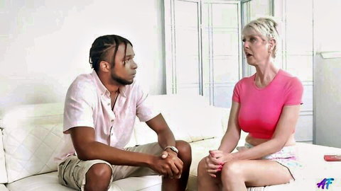 Mature blonde granny in pink top chats with black stud on couch
